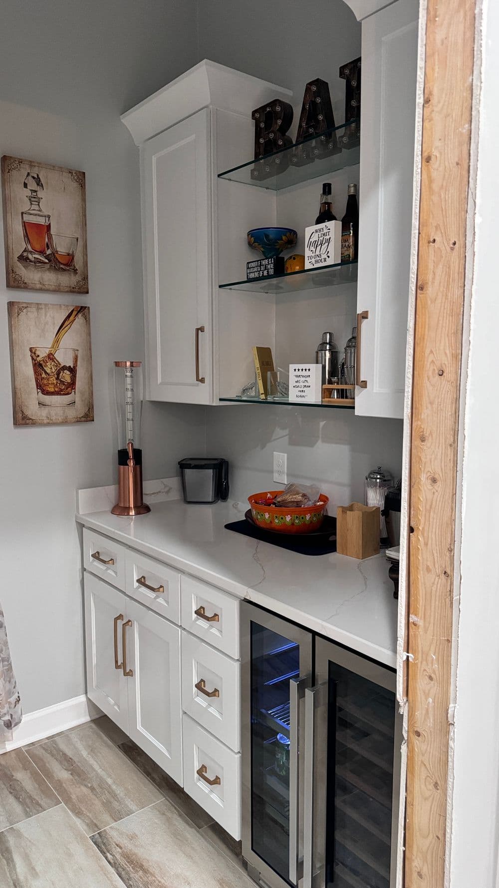 Stylish modern kitchen bar area with white cabinets, glass shelves, and beverage fridge.