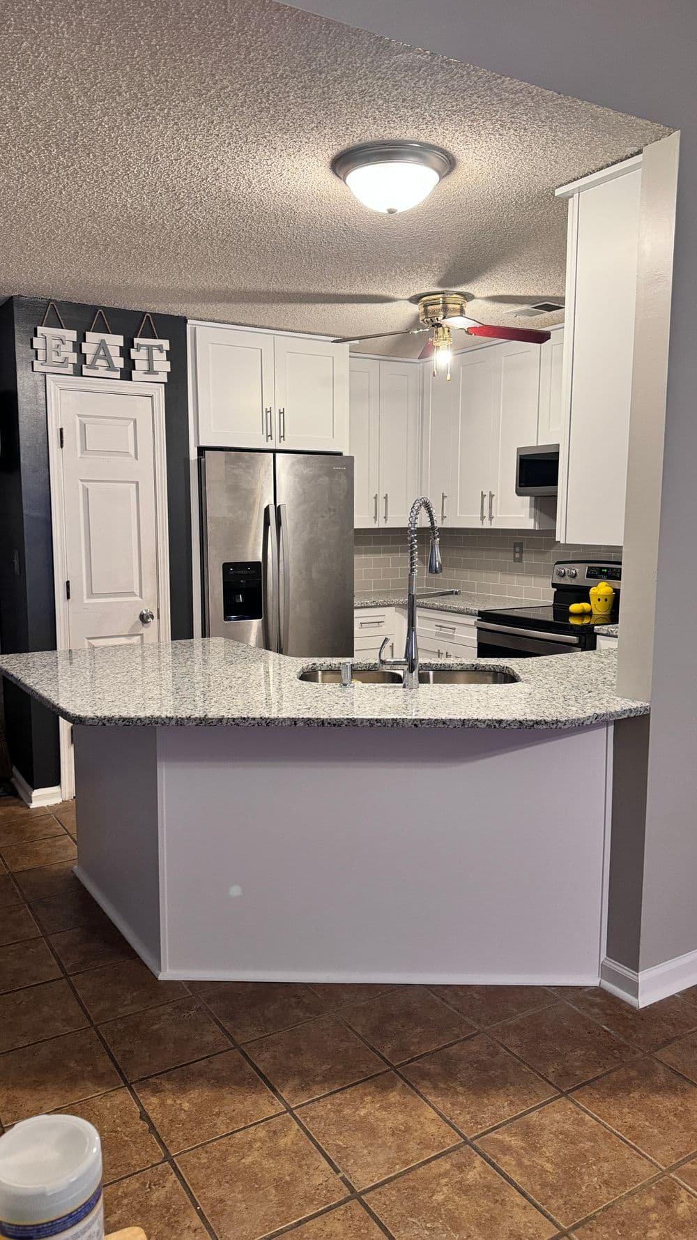 Modern kitchen with granite island, stainless steel appliances, and white cabinetry.