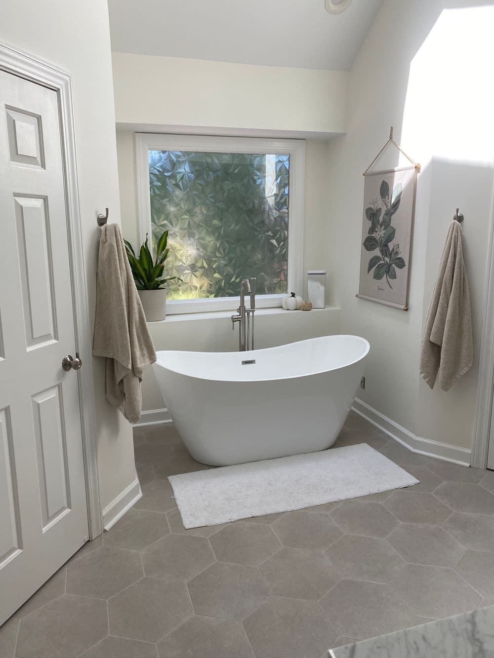 Modern bathroom with freestanding tub, natural light, and plant decor. Elegant and serene space.