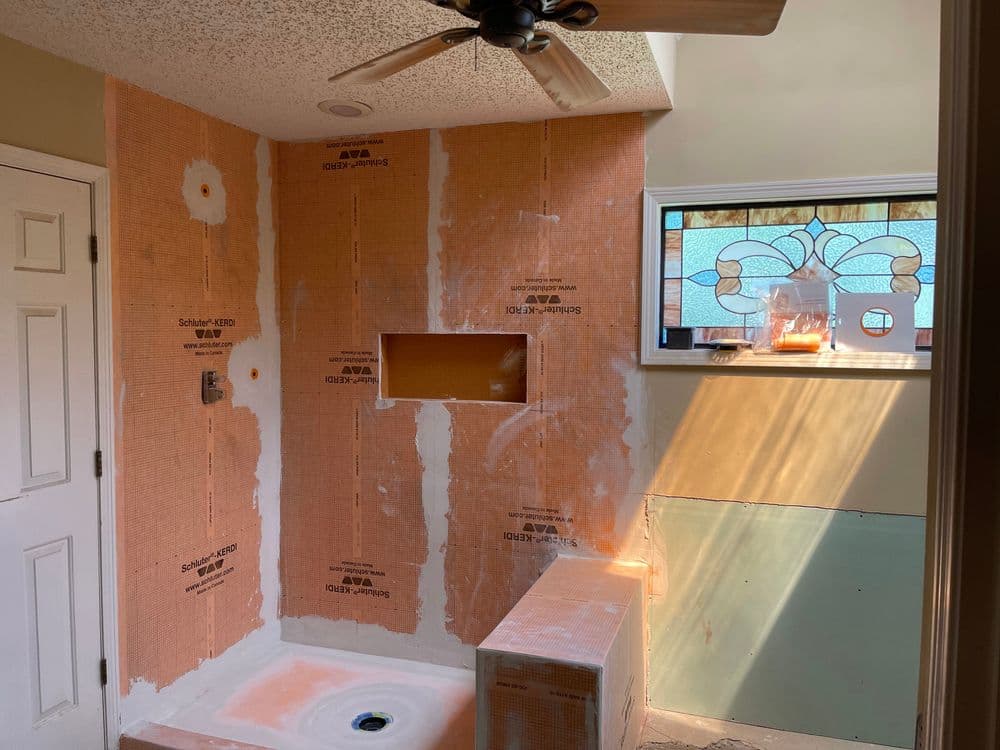 Bathroom renovation in progress with orange waterproofing, new shower space, and stained glass window.