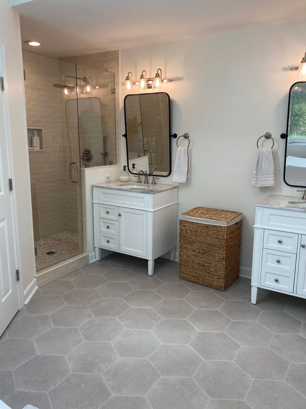 Modern bathroom featuring double sinks, hexagonal tile flooring, and a glass shower.