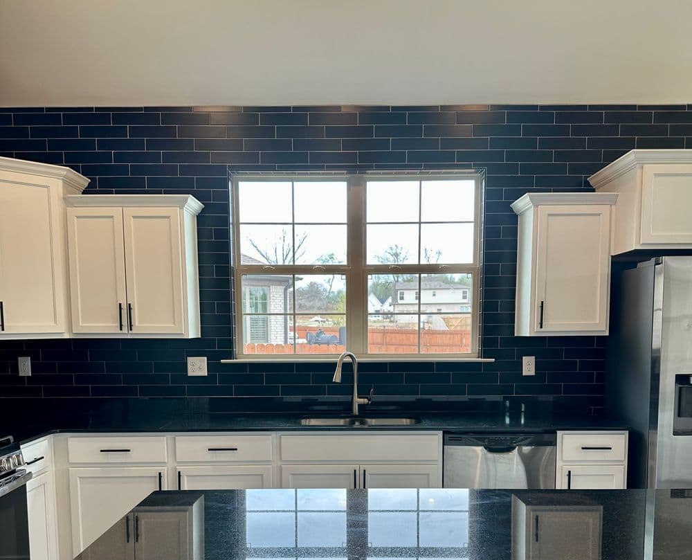 Modern kitchen with white cabinets, black countertop, and large window overlooking outdoor area.
