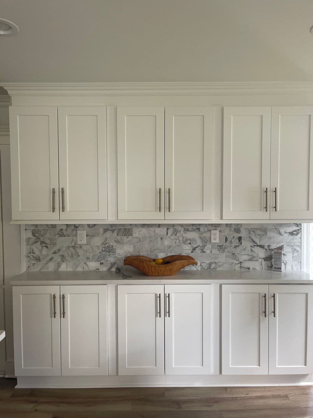 Modern kitchen featuring white cabinets, marble backsplash, and a wooden fruit bowl.