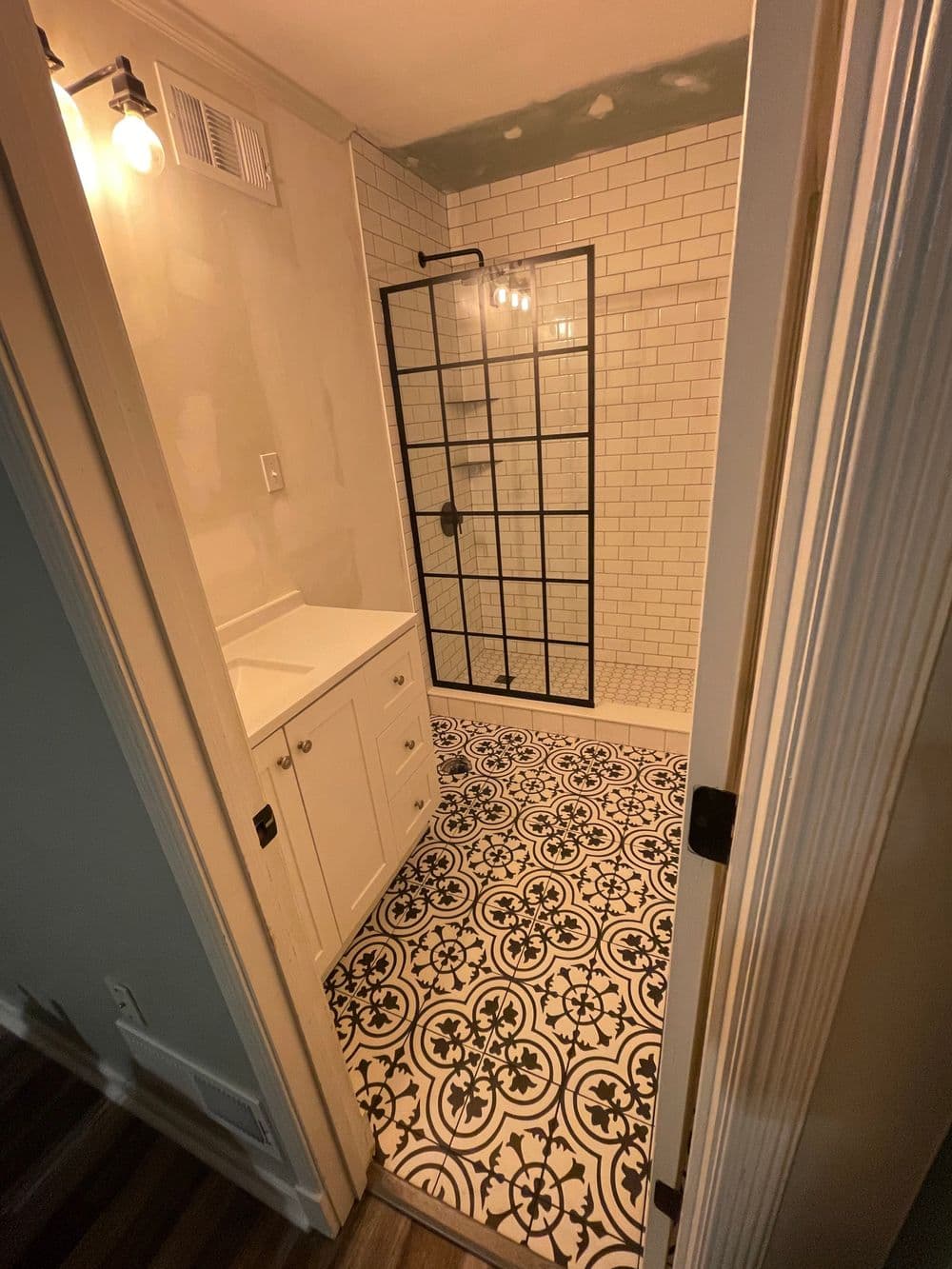 Modern bathroom with glass shower, black and white tile floor, and white cabinetry.