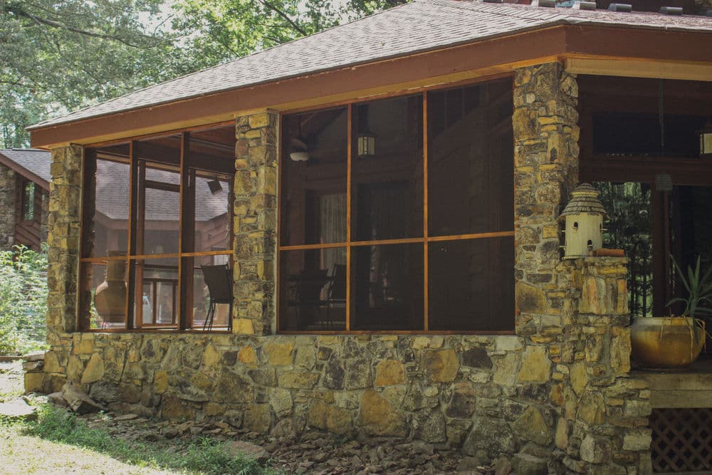 Stone screened porch with wooden accents in a serene wooded setting. Ideal for outdoor relaxation.