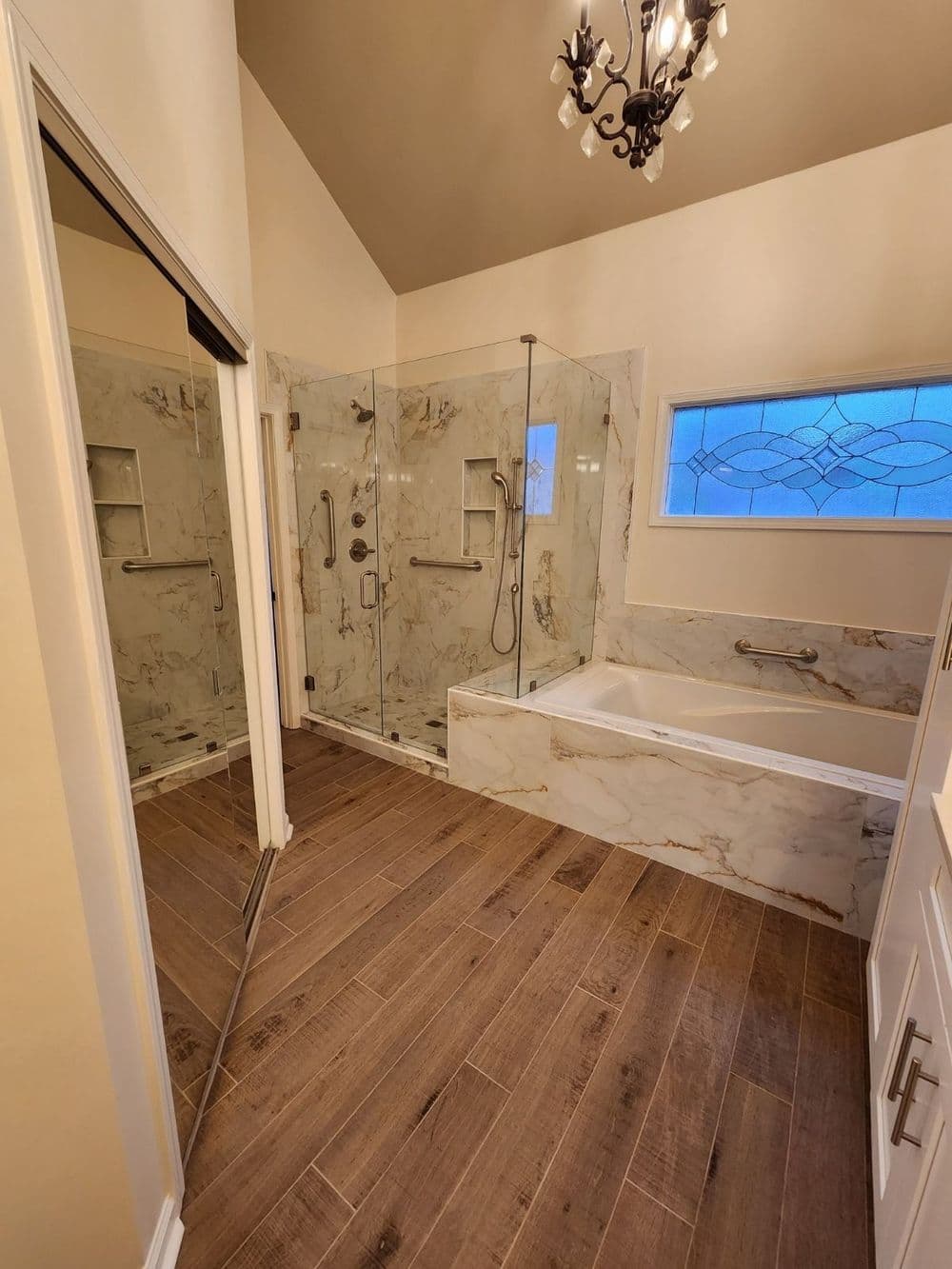 Modern bathroom with glass shower, freestanding tub, and elegant chandelier.