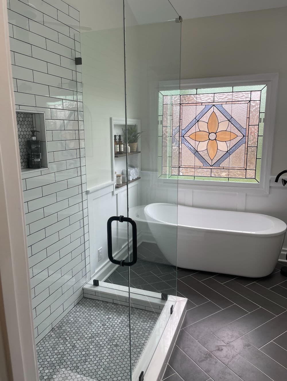 Modern bathroom featuring a glass shower, freestanding tub, and stained glass window.
