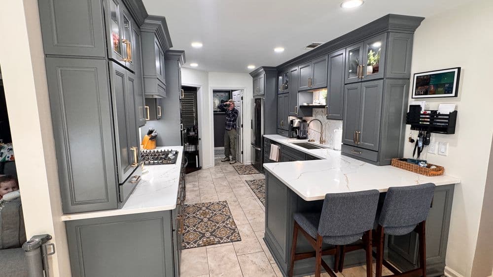 Modern gray kitchen with marble countertops, bar stools, and stainless steel appliances.