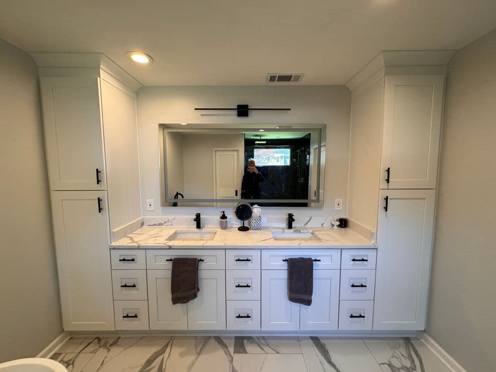 Modern bathroom with white cabinetry, marble countertops, dual sinks, and elegant fixtures.