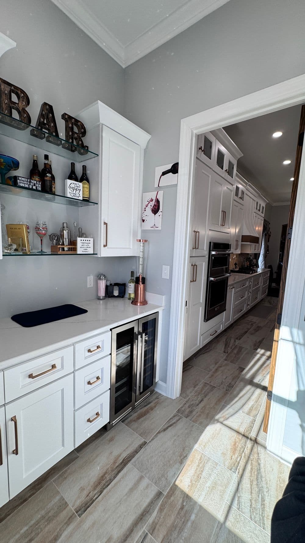 Modern kitchen featuring white cabinetry, wine cooler, and stylish bar area with decor.