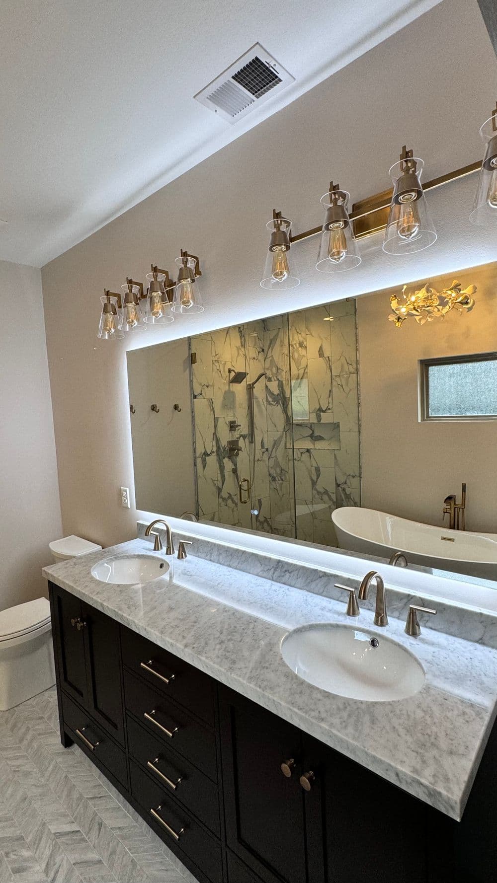 Modern bathroom with marble double vanity, stylish lighting, and glass shower enclosure.