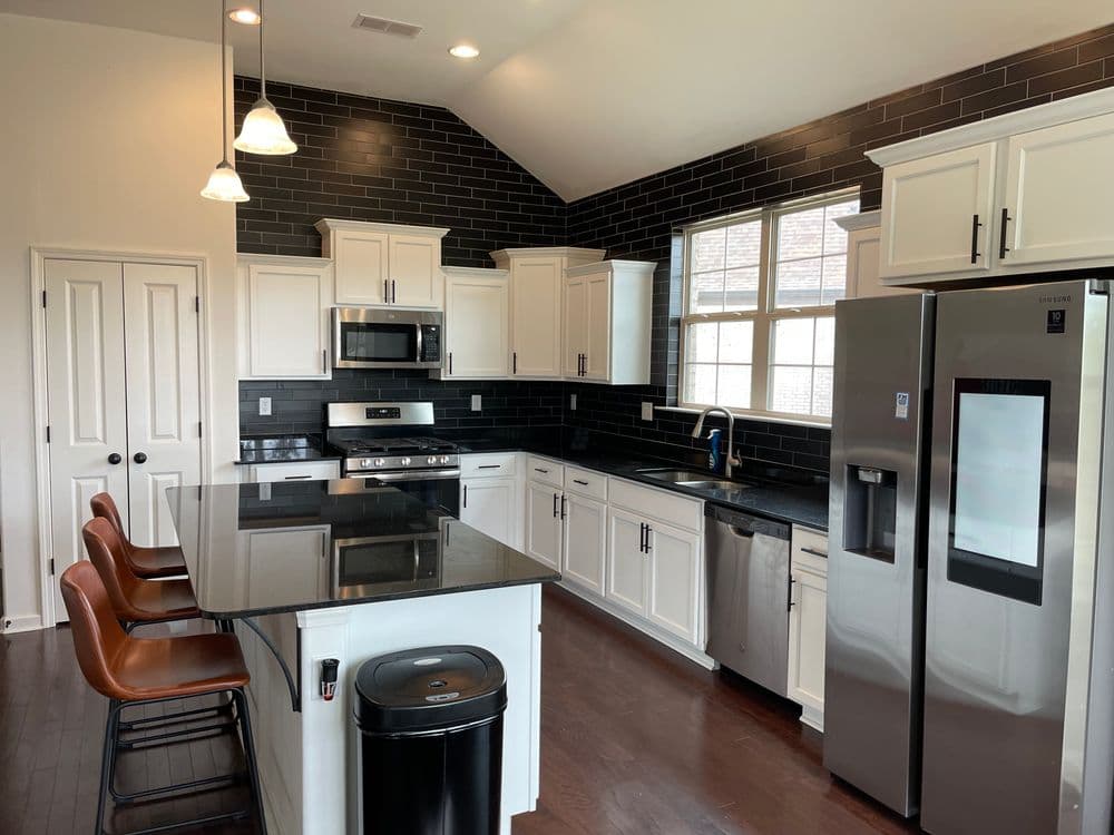 Modern kitchen with black subway tile, stainless steel appliances, and white cabinetry.