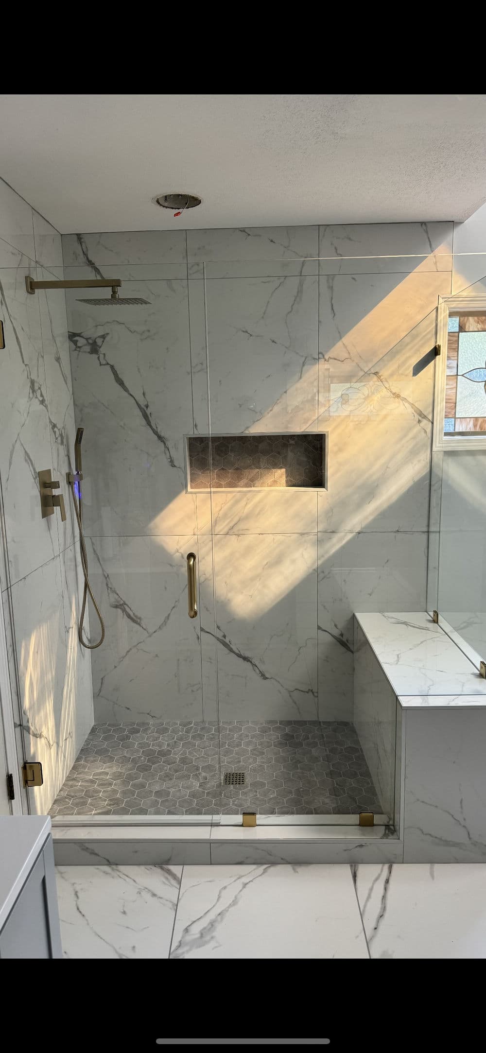 Modern bathroom shower with marble walls, glass enclosure, and stylish gold fixtures.