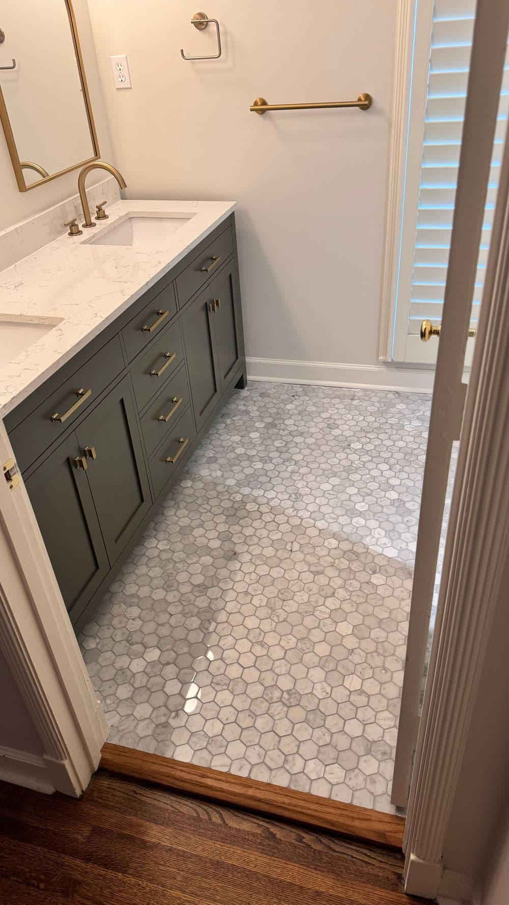 Modern bathroom with green cabinetry, marble hexagon tile floor, and stylish gold fixtures.