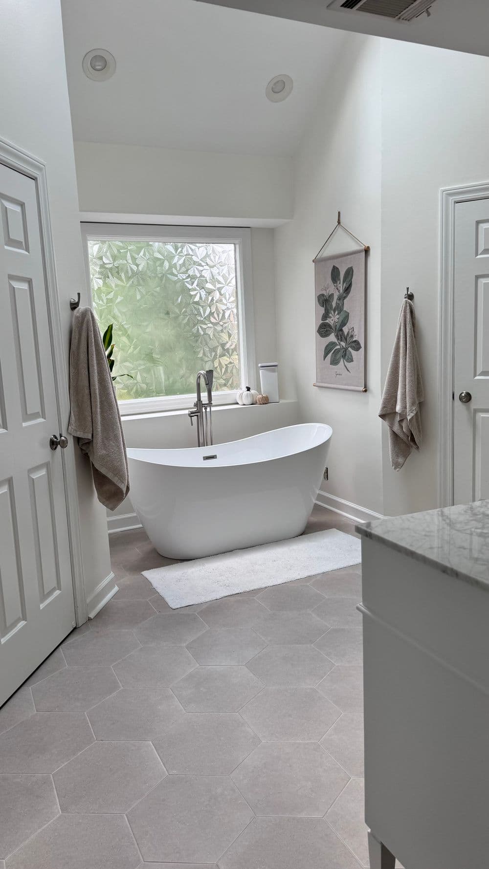 Modern bathroom featuring a freestanding bathtub, large window, and elegant decor.